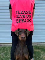 Person wearing a pink vest with 'PLEASE GIVE US SPACE' text, standing next to a dog.