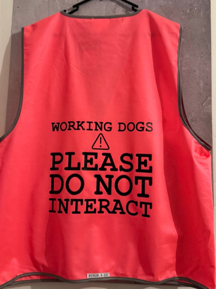 
                  
                    Pink vest with 'Working dogs please do not interact' text on a hanger.
                  
                