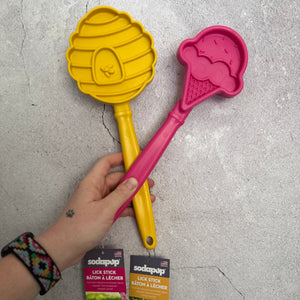 
                  
                    Yellow and pink pet trsaining tools held by a hand on a concrete floor with Sodapup packaging.
                  
                