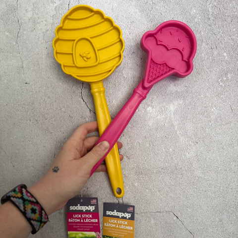 Yellow and pink pet trsaining tools held by a hand on a concrete floor with Sodapup packaging.