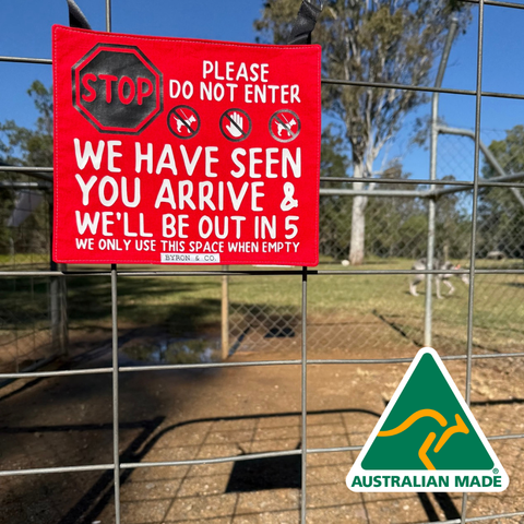 A red dog park crate sign, hanging on a gate. The sign reads 'Stop, please do not enter. We have seen you arrive, and we'll be out in 5. We only use this space when empty.' It has a black stop sign. 